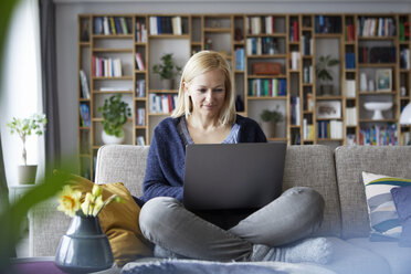 Woman at home sitting on couch using laptop - RBF06297