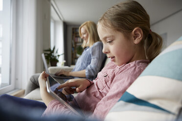 Mutter und Tochter zu Hause auf der Couch sitzend mit Laptop und Tablet - RBF06298