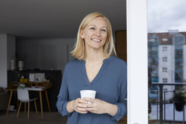 Lächelnde Frau mit einer Tasse Kaffee in der Hand und Blick aus der Balkontür - RBF06299