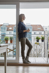 Lächelnde Frau mit einer Tasse Kaffee in der Hand und Blick aus der Balkontür - RBF06301