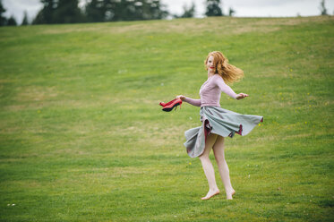 Portrait of young woman dancing in park holding red high heels - ISF09661
