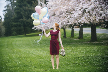 Young woman holding bunch of balloons in spring park - ISF09674