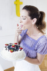 Reife Frau hält Kuchen mit Früchten, leckt Finger, Augen geschlossen - CUF31517