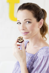 Mature woman holding sweet baked product looking at camera smiling - CUF31519