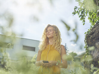 Smiling young woman with cell phone and earphones outdoors - CVF00807