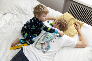 Kleiner Junge spielt mit Spielzeugauto auf der Rückseite des väterlichen T-Shirts im Bett - CUF31535