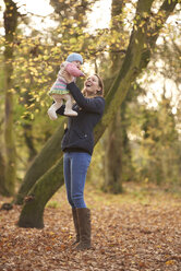 Mid adult woman holding up baby daughter in autumn park - CUF31540