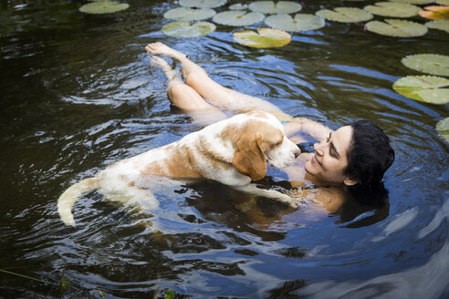 Hochformatige Ansicht einer jungen Frau mit Hund, die lächelnd zwischen Seerosenblättern schwimmt, Taiba, Ceara, Brasilien - CUF31601