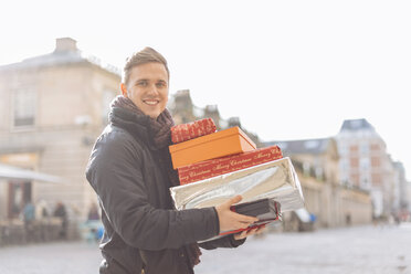 Portrait of young man carrying stack of xmas presents in Covent Garden, London, UK - CUF31663