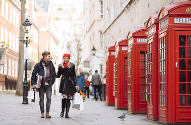 Young shopping couple strolling past red phone boxes, London, UK - CUF31680