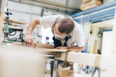 Young man in workshop looking down counting plywood sheets - CUF31710