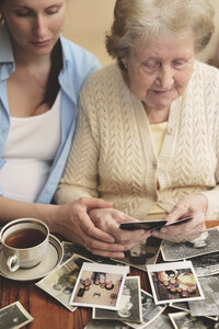 Ältere Frau und Enkelin sitzen am Tisch und sehen sich alte Fotos an - CUF31716