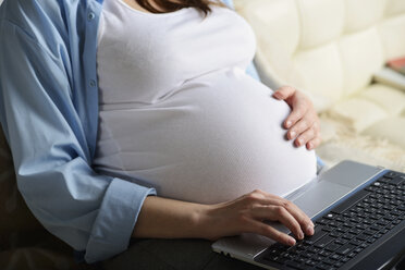 Schwangere Frau auf dem Sofa sitzend, mit Laptop, Mittelteil - CUF31738