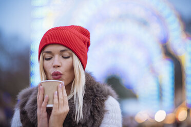 Junge Frau, die auf dem Weihnachtsfest im Hyde Park, London, UK, Glühwein bläst - CUF31761