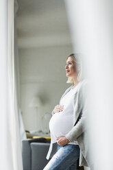 Hochschwangere junge Frau, die aus dem Fenster blickt - CUF31784