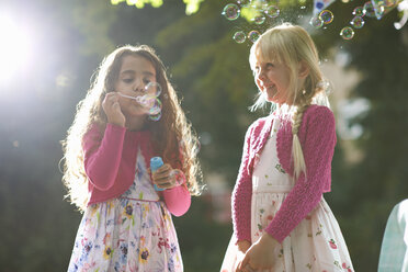 Zwei süße Mädchen blasen Seifenblasen im sonnenbeschienenen Garten - CUF31810