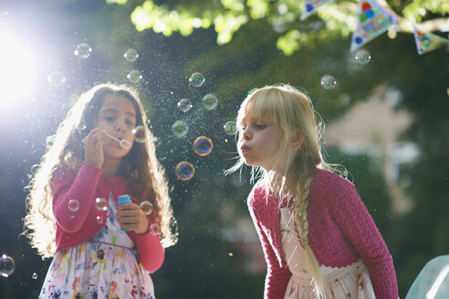 Two girls blowing bubbles in sunlit garden - CUF31811