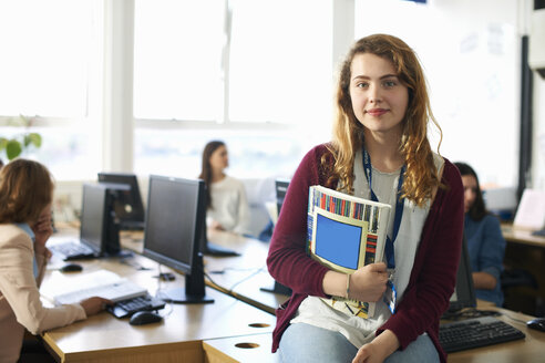 Porträt einer Studentin, die vor einer Computerklasse eine Datei hält - CUF31822