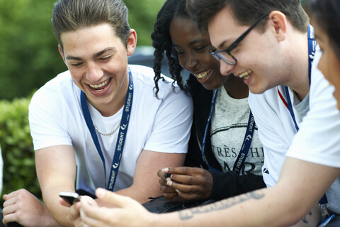 Männliche und weibliche Studenten auf dem College-Campus lesen Smartphone-Nachrichten, lizenzfreies Stockfoto