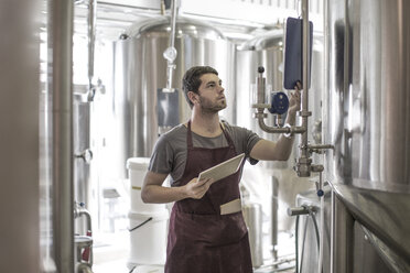 Brewers in brewery standing next to stainless steel tanks - ISF09727