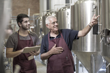 Brewers in brewery standing next to stainless steel tanks - ISF09728
