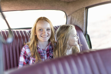 Two young girls sitting in back seat of car, smiling - ISF09752