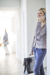 Mid adult businesswoman chatting on smartphone in hotel corridor - ISF09768