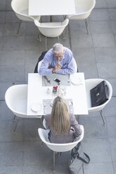 Blick von oben auf einen älteren Geschäftsmann und eine Frau, die sich am Tisch auf der Hotelterrasse unterhalten - ISF09791