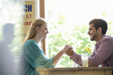 Side view of couple holding hands across table, looking at each other smiling - CUF31853