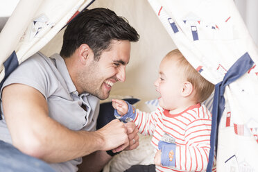 Father and young son sitting in play tent indoors, laughing together - CUF31882