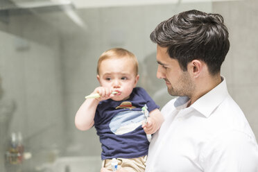 Father holding young son while son brushes teeth - CUF31894