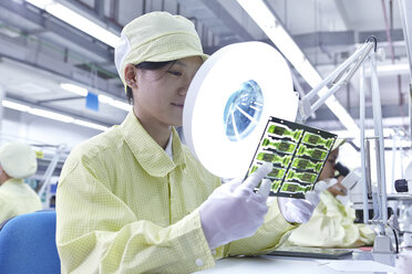 Arbeiterin mit Lupe bei der Qualitätskontrolle in einer Fabrik, die flexible elektronische Leiterplatten herstellt. Die Fabrik befindet sich im Süden Chinas, in Zhuhai, Provinz Guangdong - CUF31969