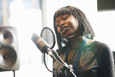 Head and shoulders of young woman singing into microphone through pop guard - CUF32106