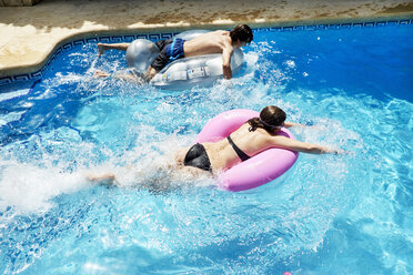 Junger Mann und Schwester im Teenageralter rasen auf Hüpfburgen im Schwimmbad - CUF32129