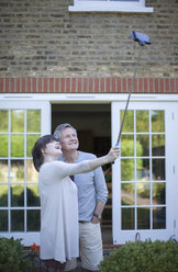 Father and grown daughter in garden taking a self portrait, using a selfie stick - CUF32187