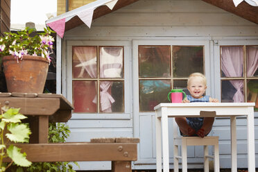 Baby girl sitting at table in front of playhouse looking at camera smiling - CUF32220