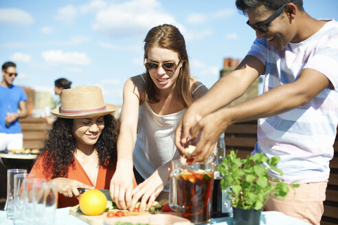 Adult friends preparing fruit for punch cocktail at rooftop party - CUF32243