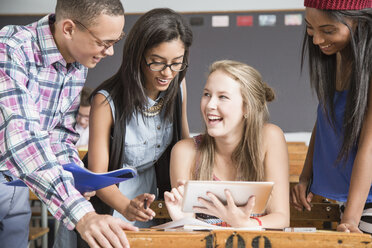 Gruppe von Schülern im Klassenzimmer, die auf ein digitales Tablet schauen - CUF32258