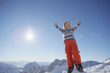 Young boy standing in snowy landscape, celebrating with arms raised, low angle view - ISF09886