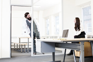 Young man leaning into office talking to woman - ISF09928