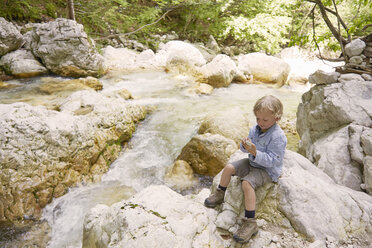 Boy sitting on rocks by woodland river, Bovec, Soca, Slovenia - ISF09995