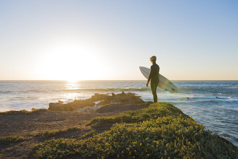 Junger männlicher Surfer, der bei Sonnenaufgang von einer Klippe aufs Meer hinausschaut - ISF10062