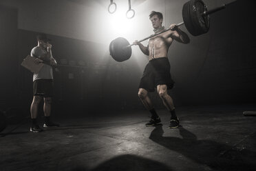 Mid adult man lifting barbell, while trainer looks on, low angle view - ISF10118