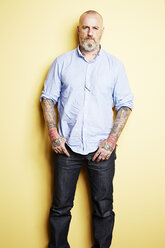 Mature man with tattoos on arms and neck, yellow background - ISF10158
