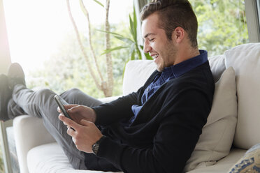 Portrait of man relaxing on sofa with feet up looking at digital reading device - ISF10184