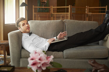 Portrait of man wearing smart clothes laying on sofa using laptop - ISF10189