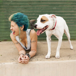 Young woman with colourful hair, lying on floor next to dog, laughing - ISF10193