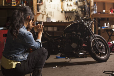 Mechanikerin in der Werkstatt, die mit ihrem Smartphone ein Motorrad fotografiert - ISF10207