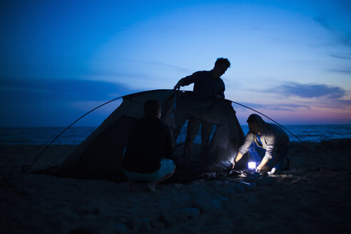 Eine Gruppe von Freunden baut bei Sonnenuntergang ihr Zelt am Strand auf - ISF10285
