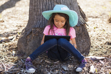 Nettes Mädchen lehnt an einem Baumstamm und benutzt ein digitales Tablet - ISF10317